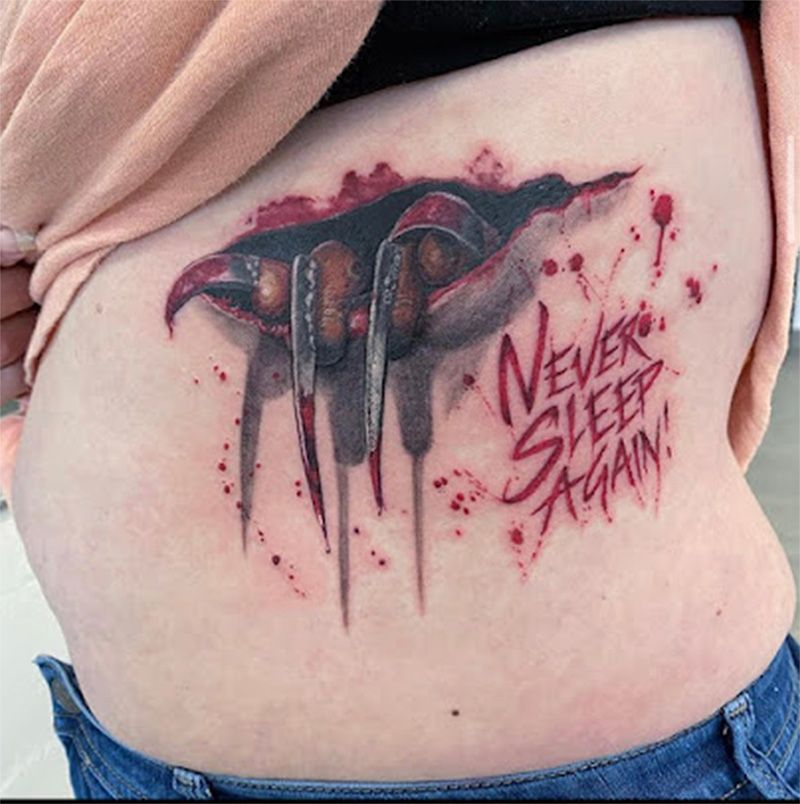 Tattoo on torso of Freddy Krueger's claw reaching through torn skin, splattered blood, text 