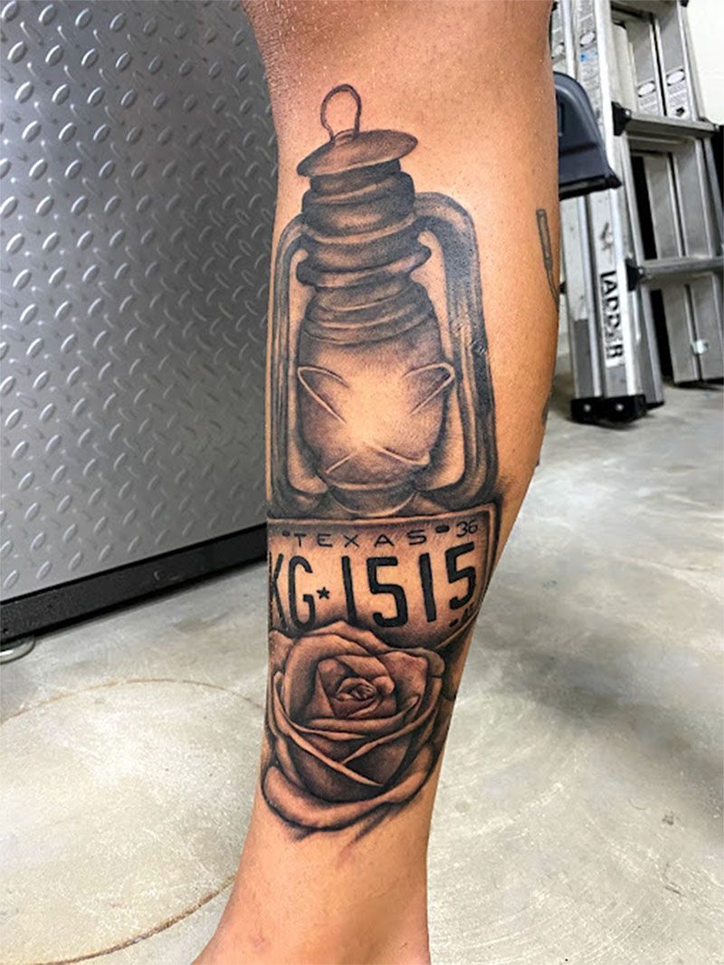 A person has a tattoo of a lantern and roses on their leg.