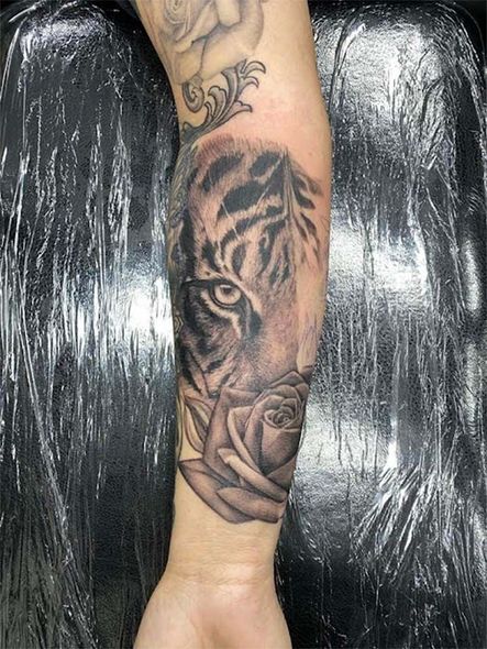 A person has a tattoo of a tiger and a rose on their forearm.