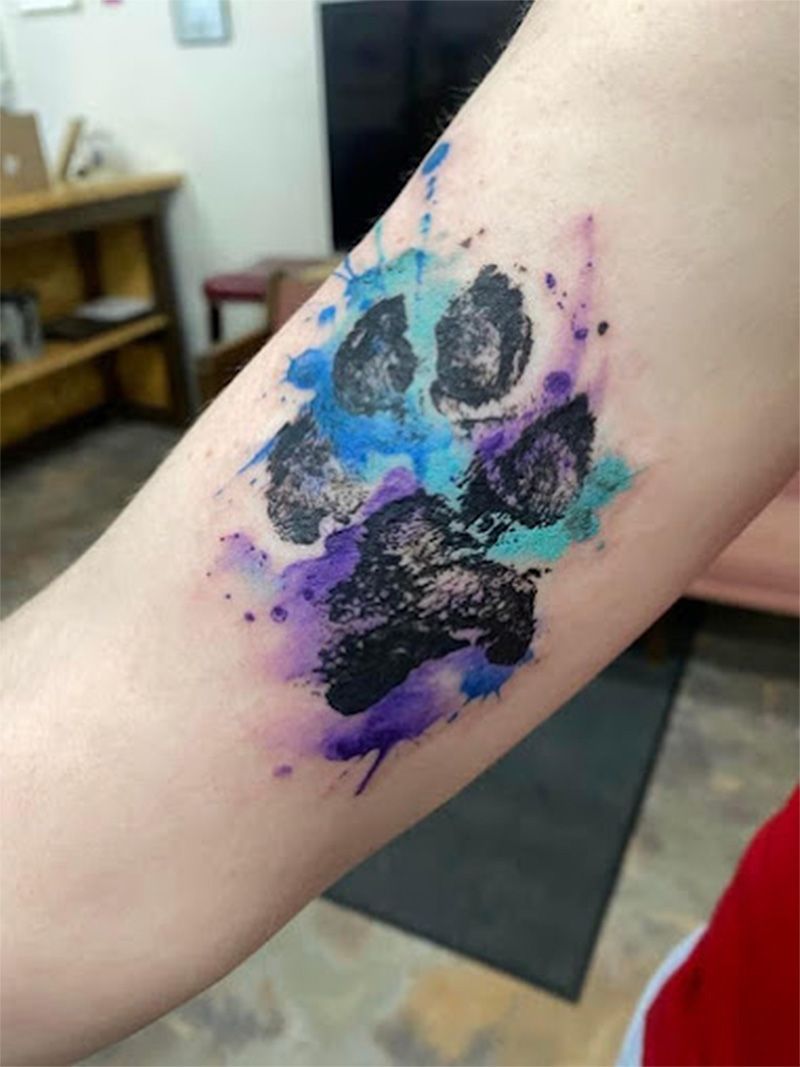 A person has a watercolor paw print tattoo on their arm.