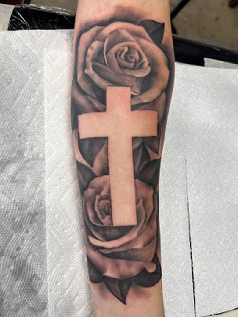 A tattoo of a cross and roses on a person 's arm