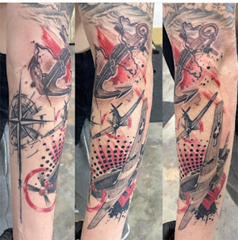 A tattoo of an airplane anchor and compass on a person 's arm