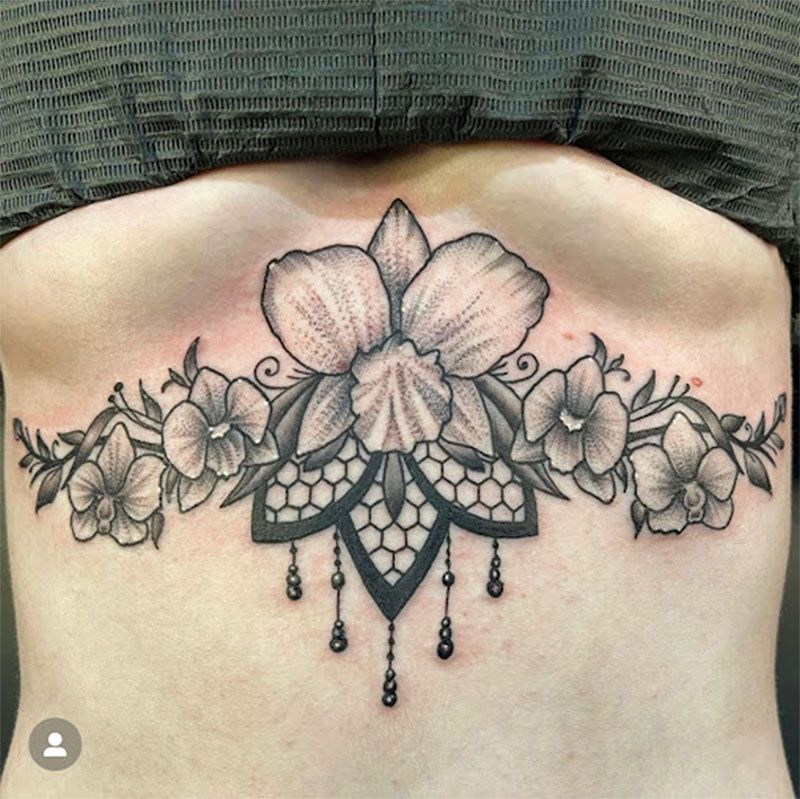 A woman has a tattoo of flowers and lace on her chest