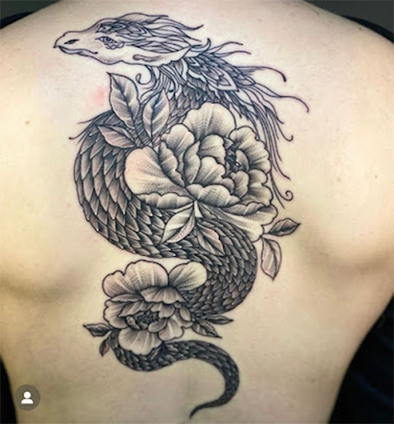 A person has a tattoo of a dragon with flowers on their back