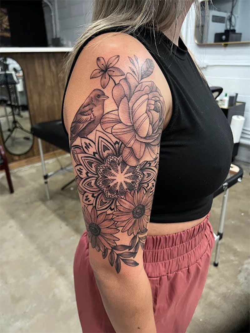 A woman has a tattoo of flowers and birds on her arm.