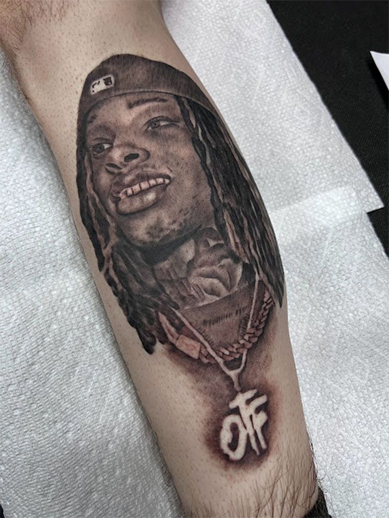 A black and white tattoo of a man with dreadlocks on his leg.