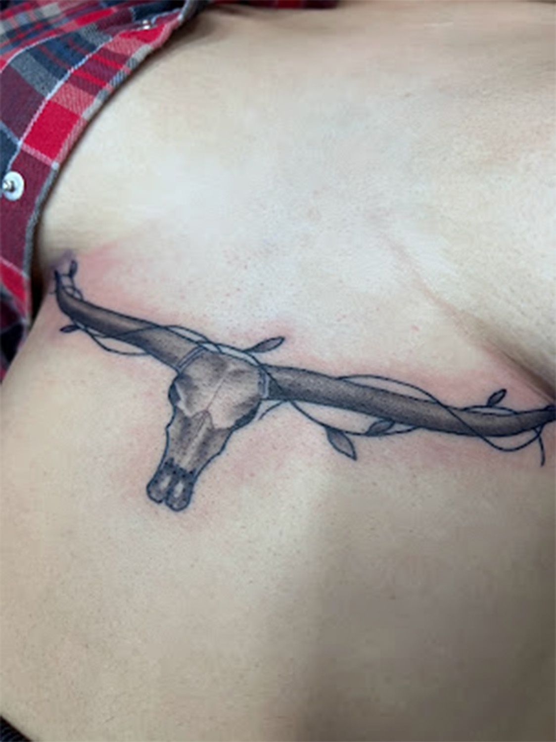 A woman has a tattoo of a bull 's skull on her chest.