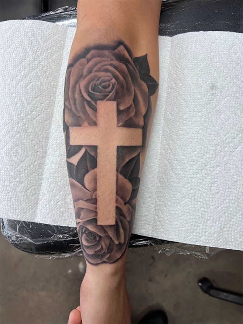 A person has a tattoo of a cross and roses on their leg.