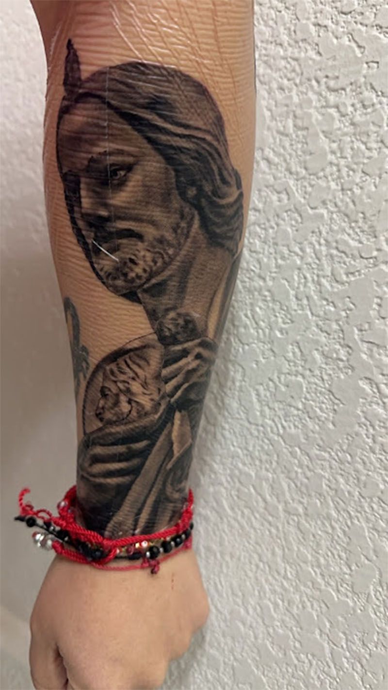 A person has a tattoo of jesus on their forearm.