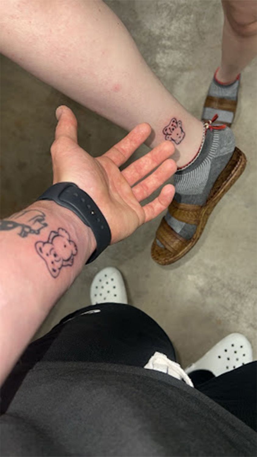 A person with a tattoo on their arm is reaching out to another person with a tattoo on their ankle.