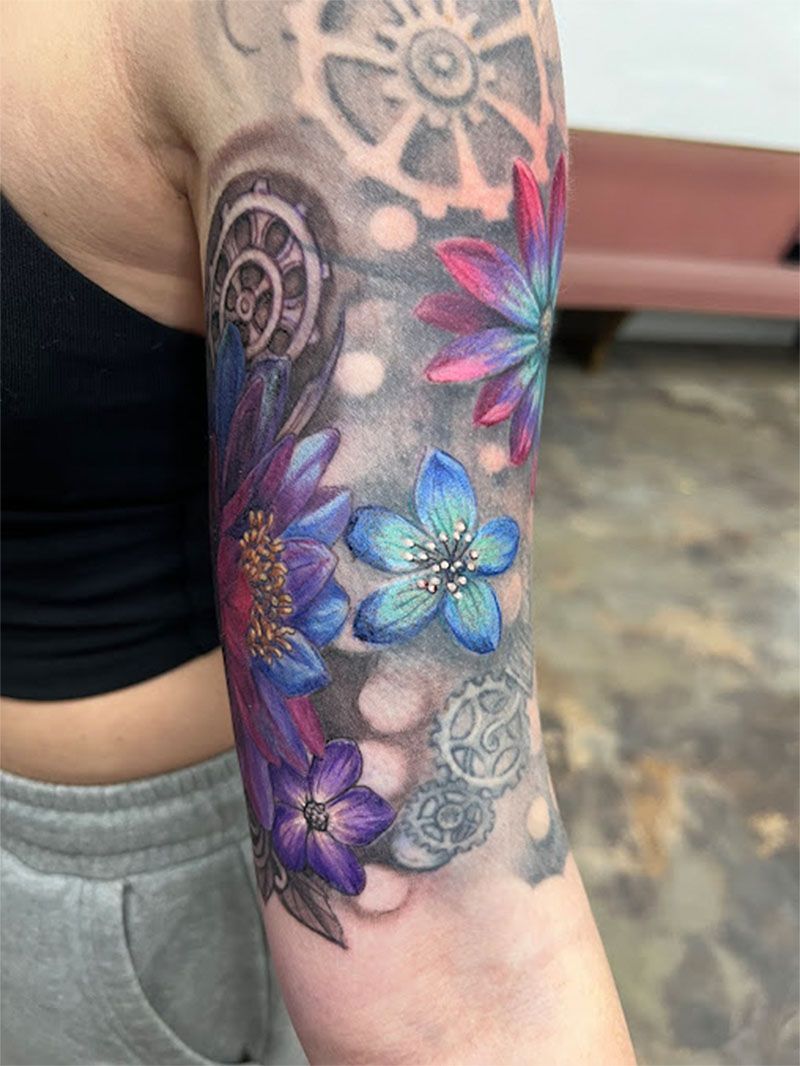 A woman has a tattoo of flowers and gears on her arm.