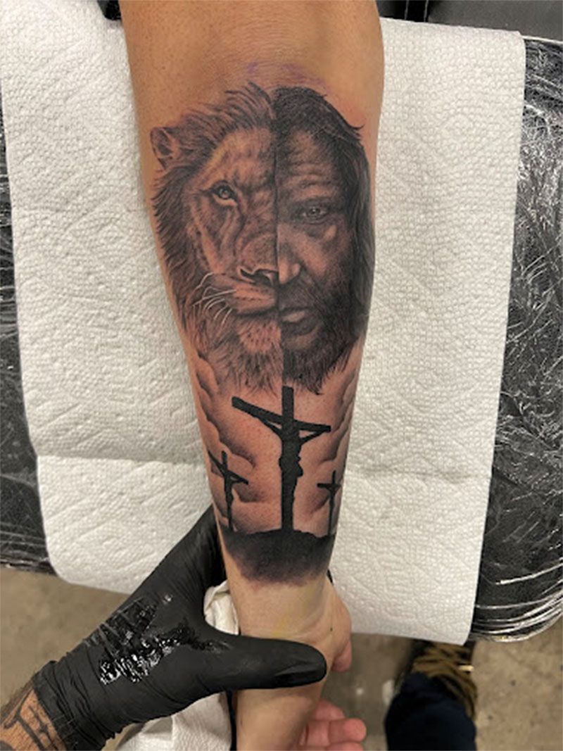 A person has a tattoo of a lion and jesus on their forearm.