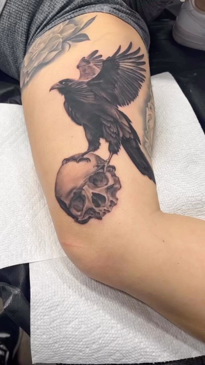 A person has a tattoo of a crow sitting on a skull on their arm.