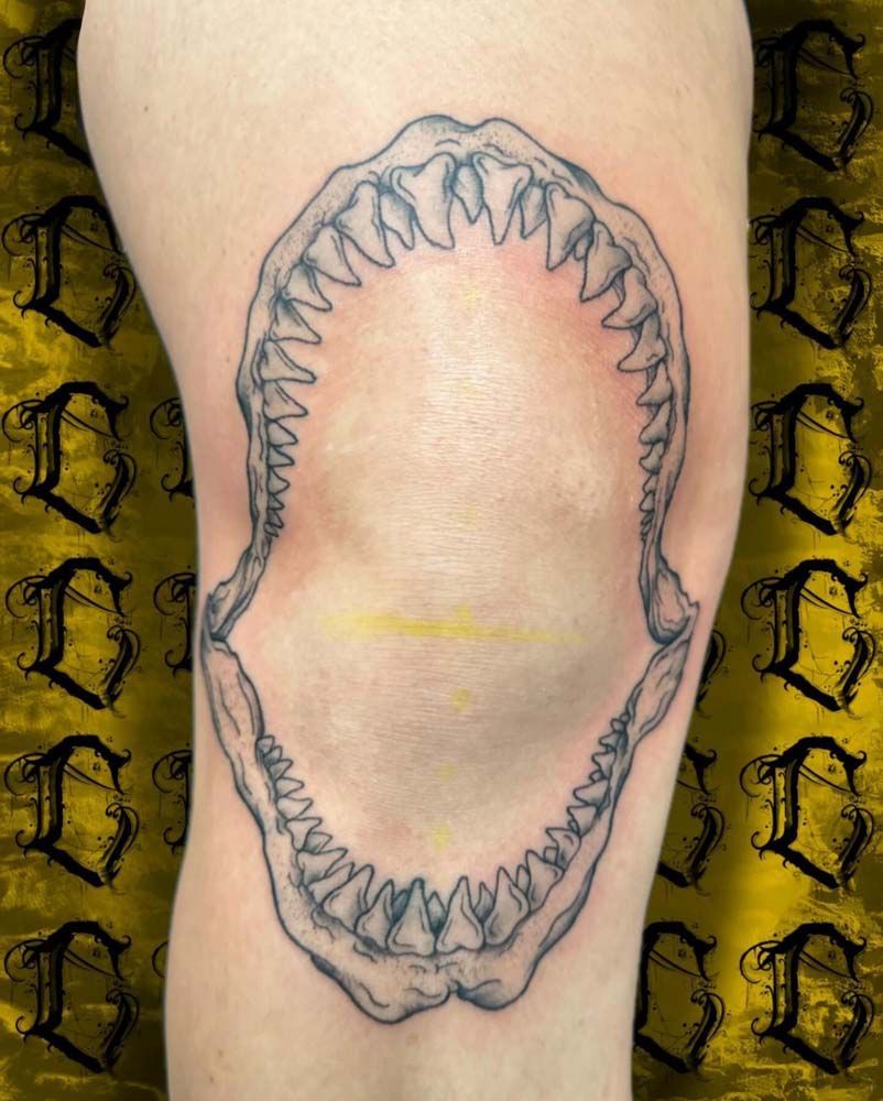 A person has a shark tooth tattoo on their knee