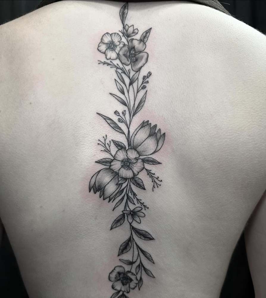 A woman has a black and white tattoo of flowers on her back.