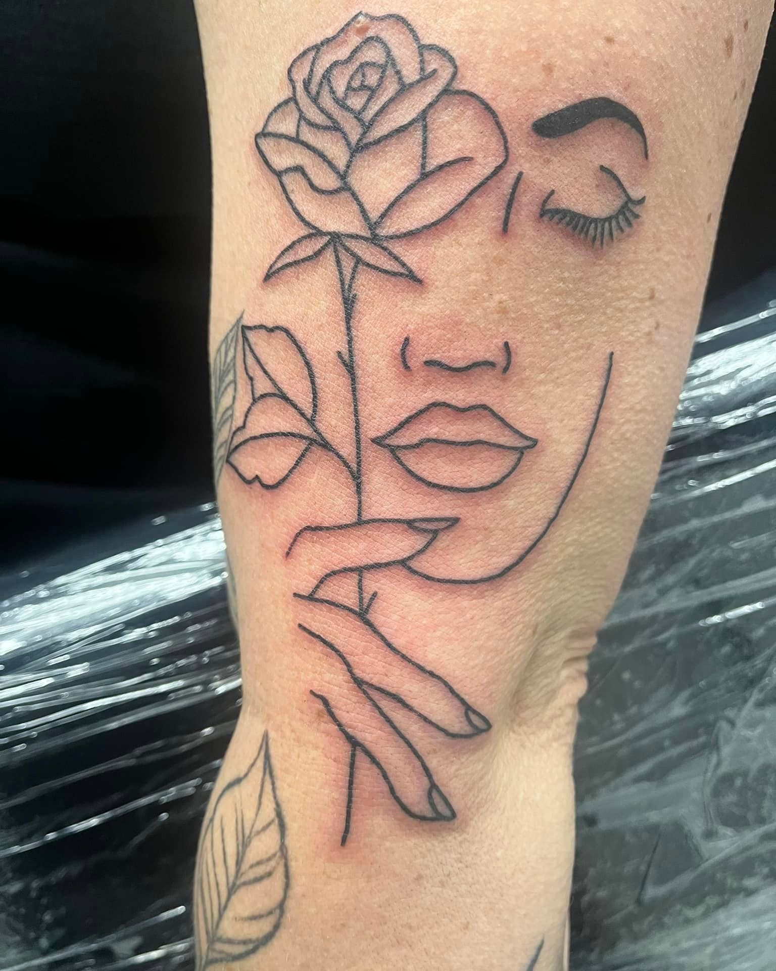 A tattoo of a woman 's face with a rose and a hand