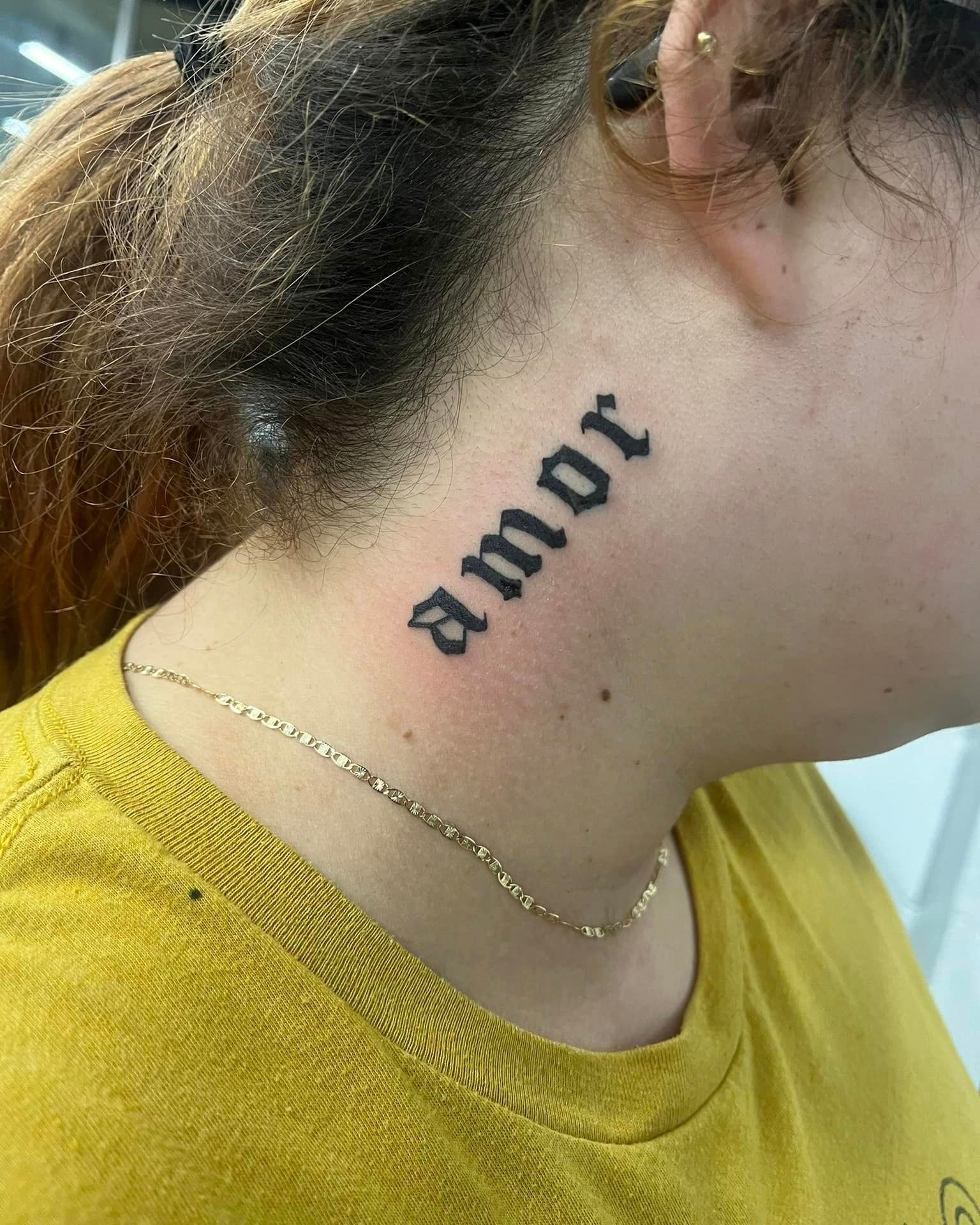 A woman has a tattoo of the word amor on her neck.