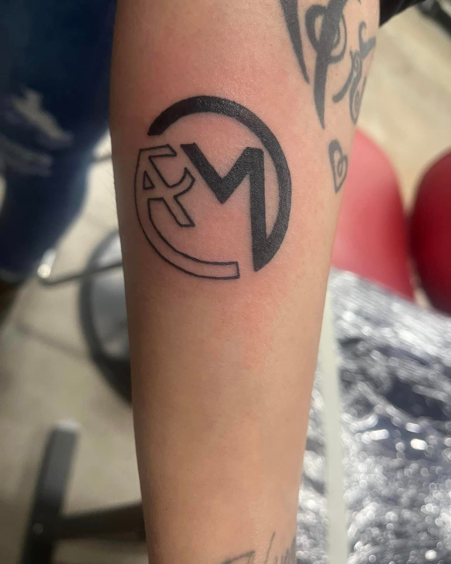 A person has a tattoo of a letter m on their forearm