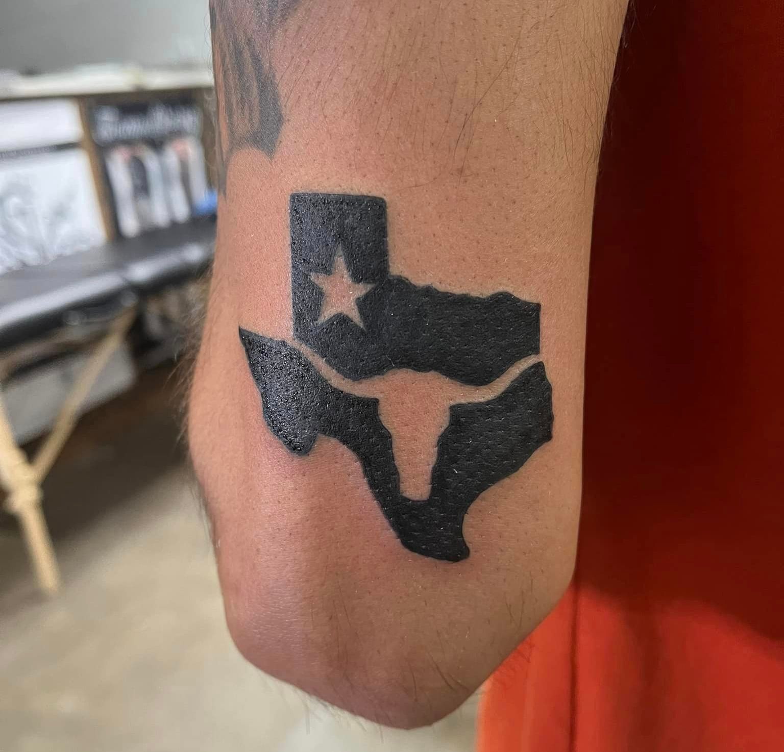 A man has a tattoo of the state of texas on his elbow.