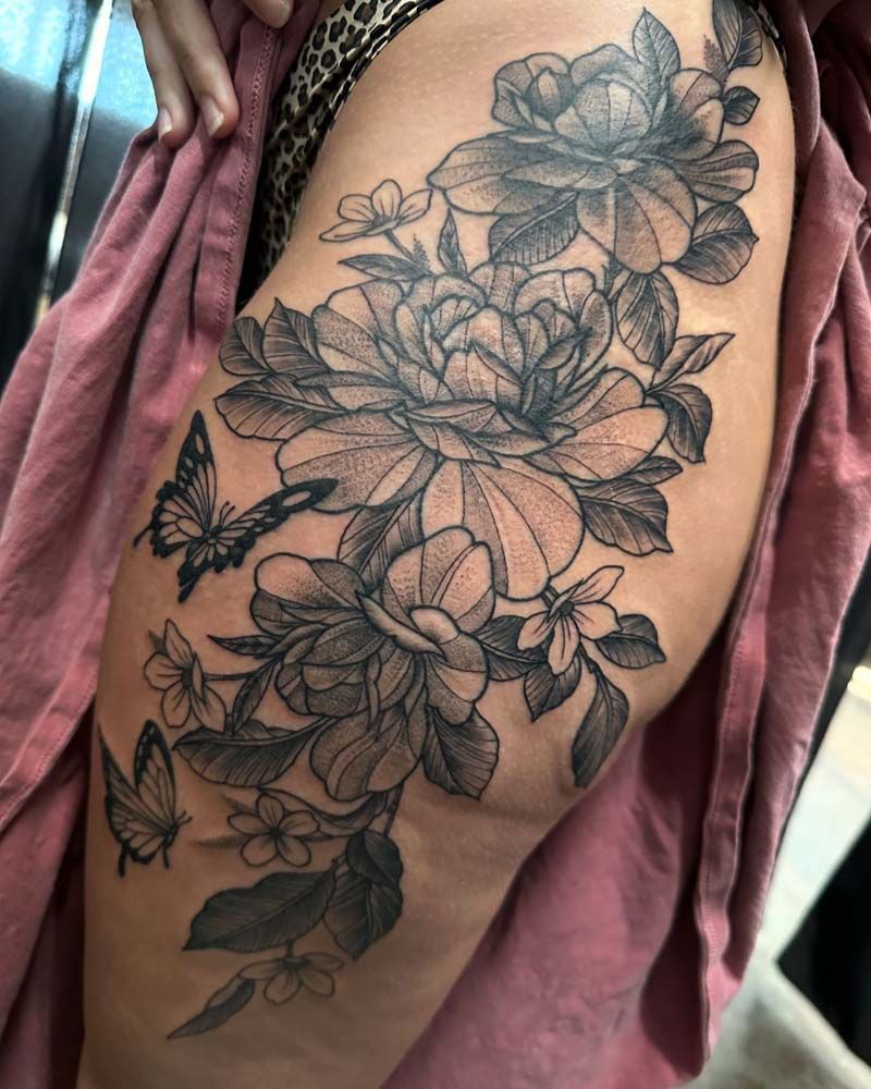 A woman has a tattoo of flowers and butterflies on her thigh.