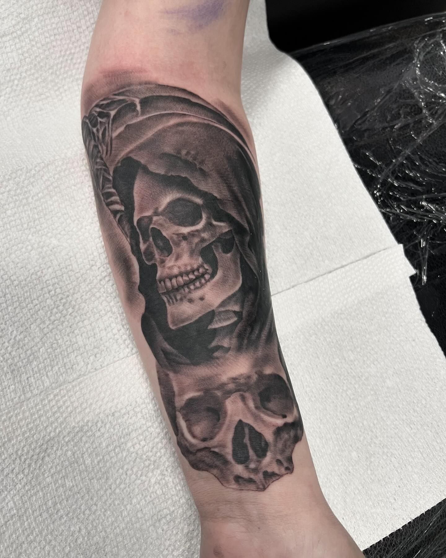 A person has a grim reaper tattoo on their forearm.