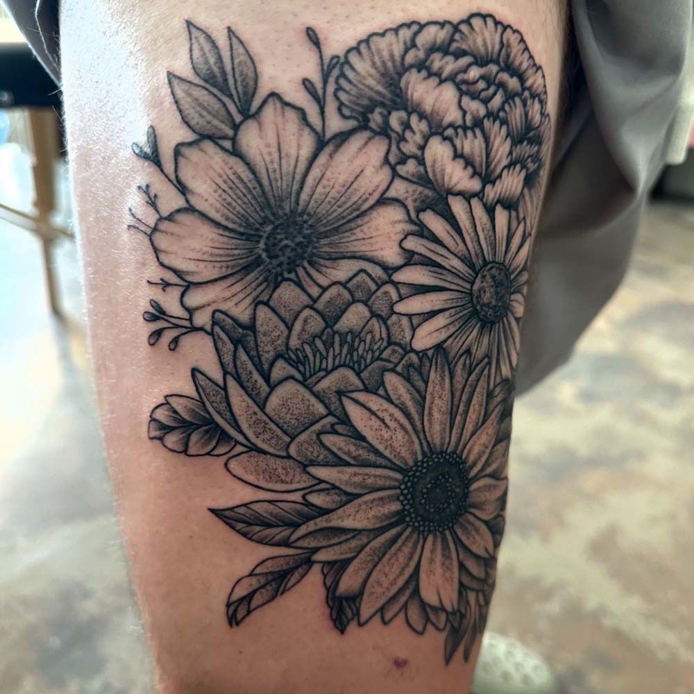 A black and white tattoo of flowers on a person 's leg.