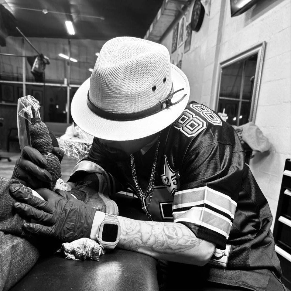 A man wearing a hat is getting a tattoo on another man 's arm