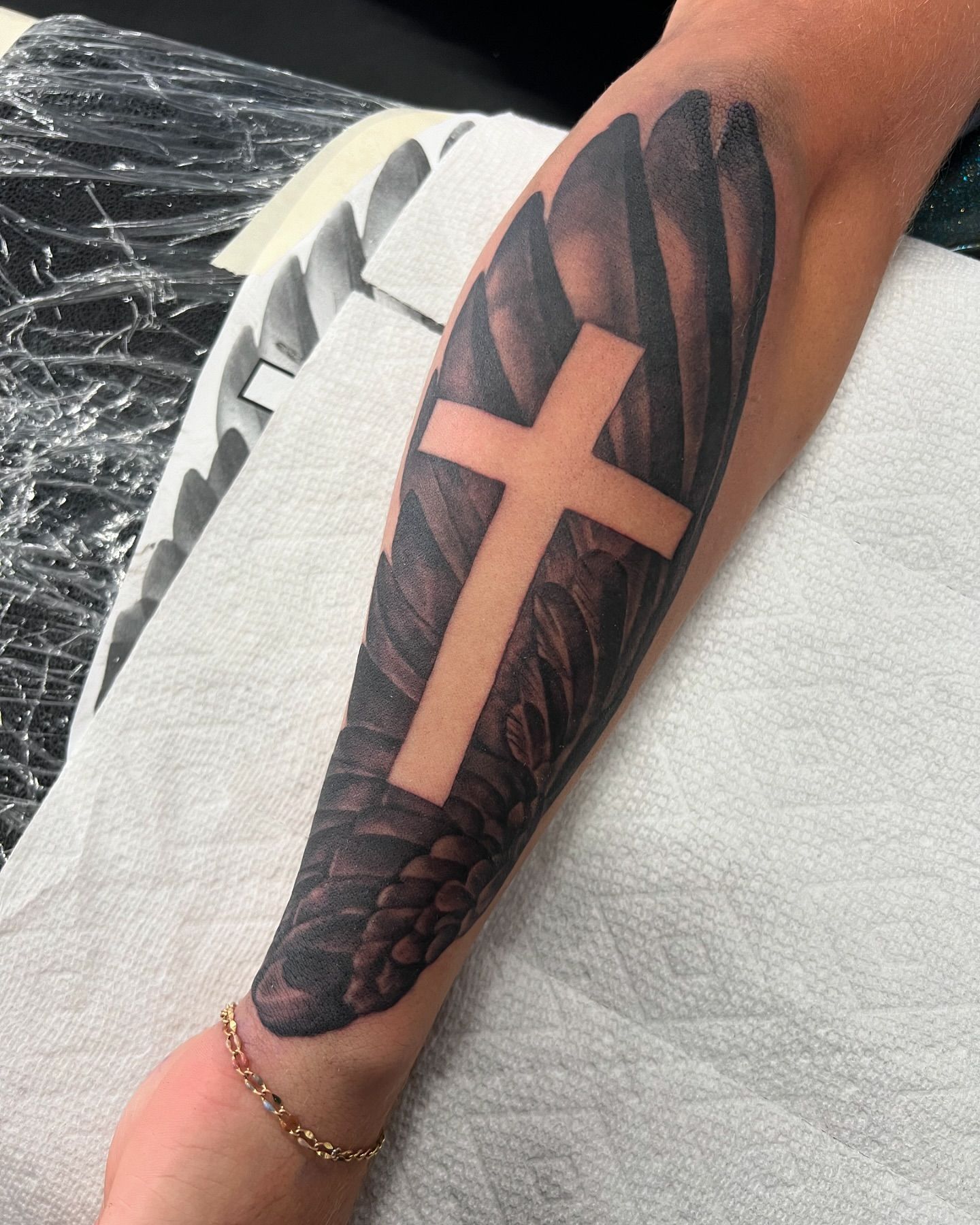 A person has a tattoo of a cross and wings on their arm.