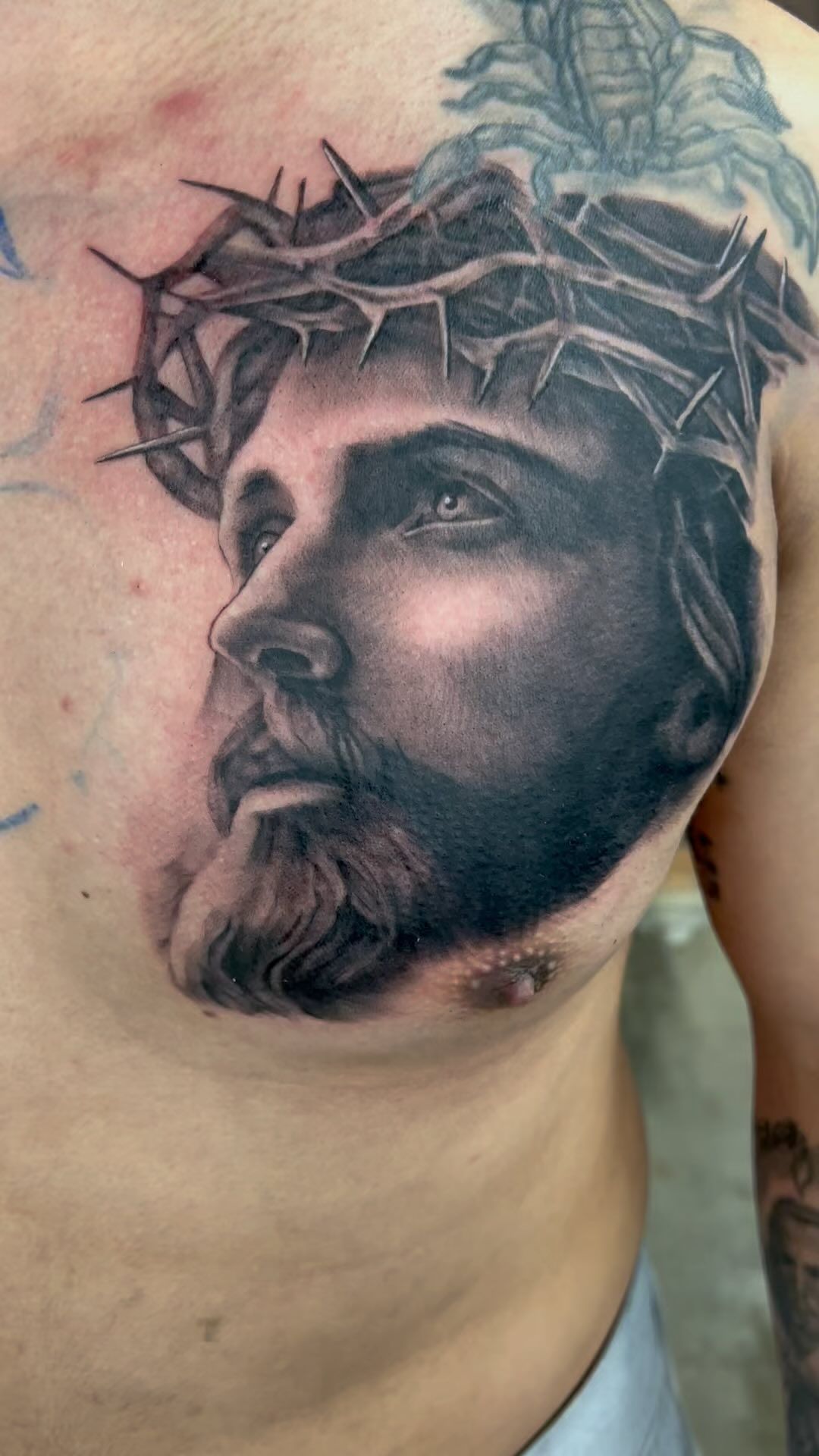 A man has a tattoo of jesus with a crown of thorns on his chest.