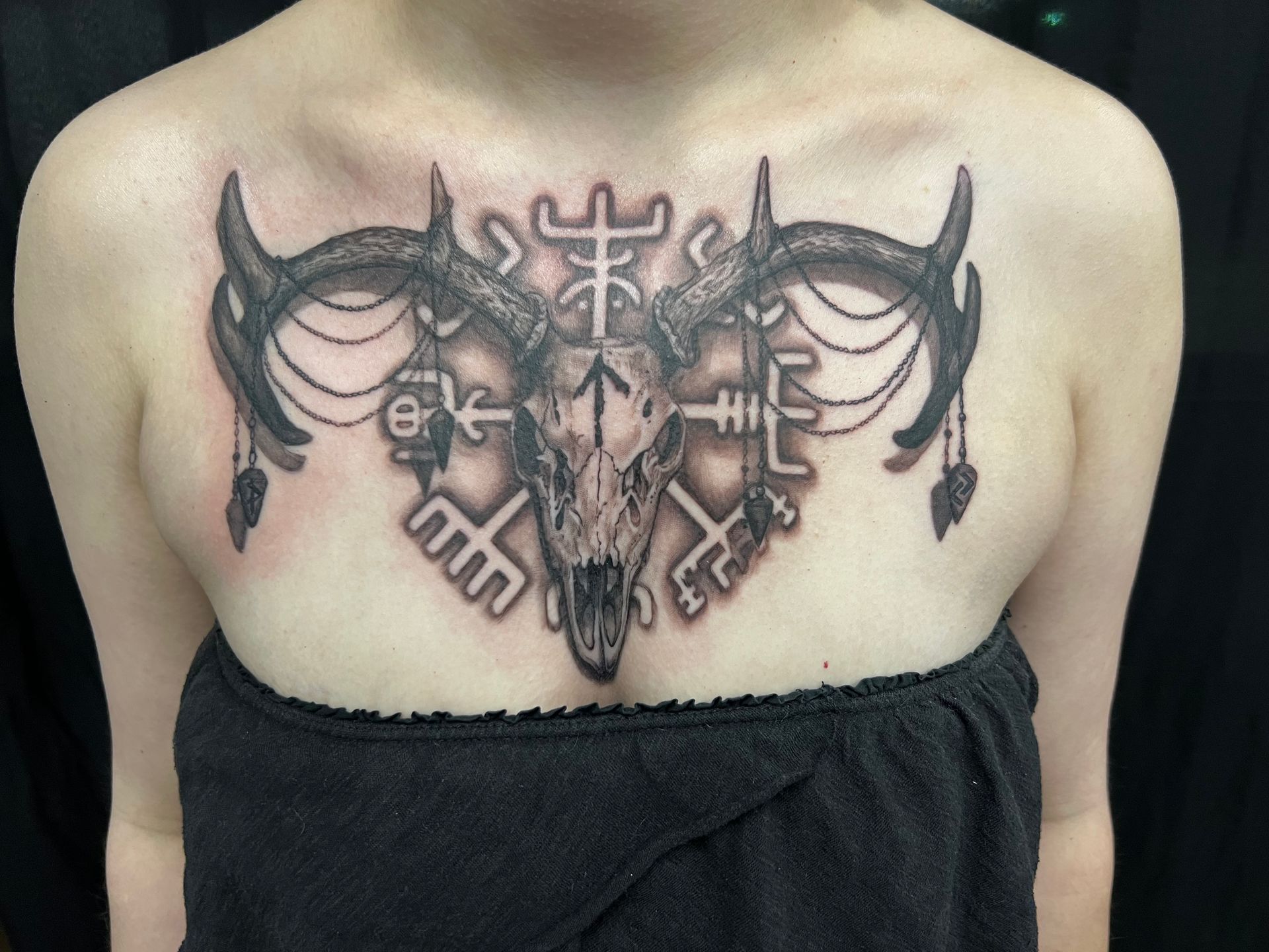 Tattoo of a ram skull with antlers and runes on a person's chest.