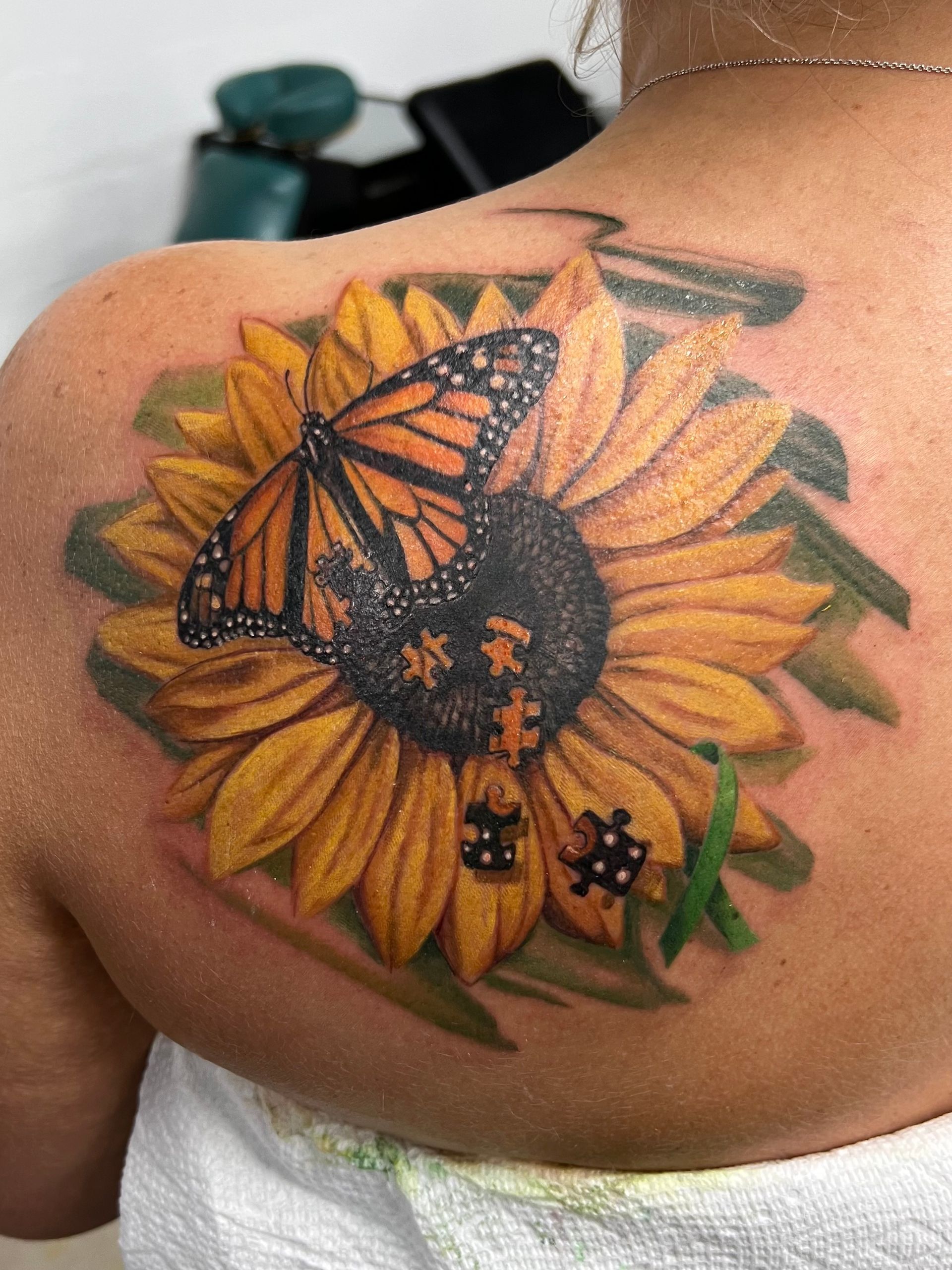 Sunflower tattoo with a butterfly, jigsaw pieces, and ladybug. Yellow, orange, black, and green colors.