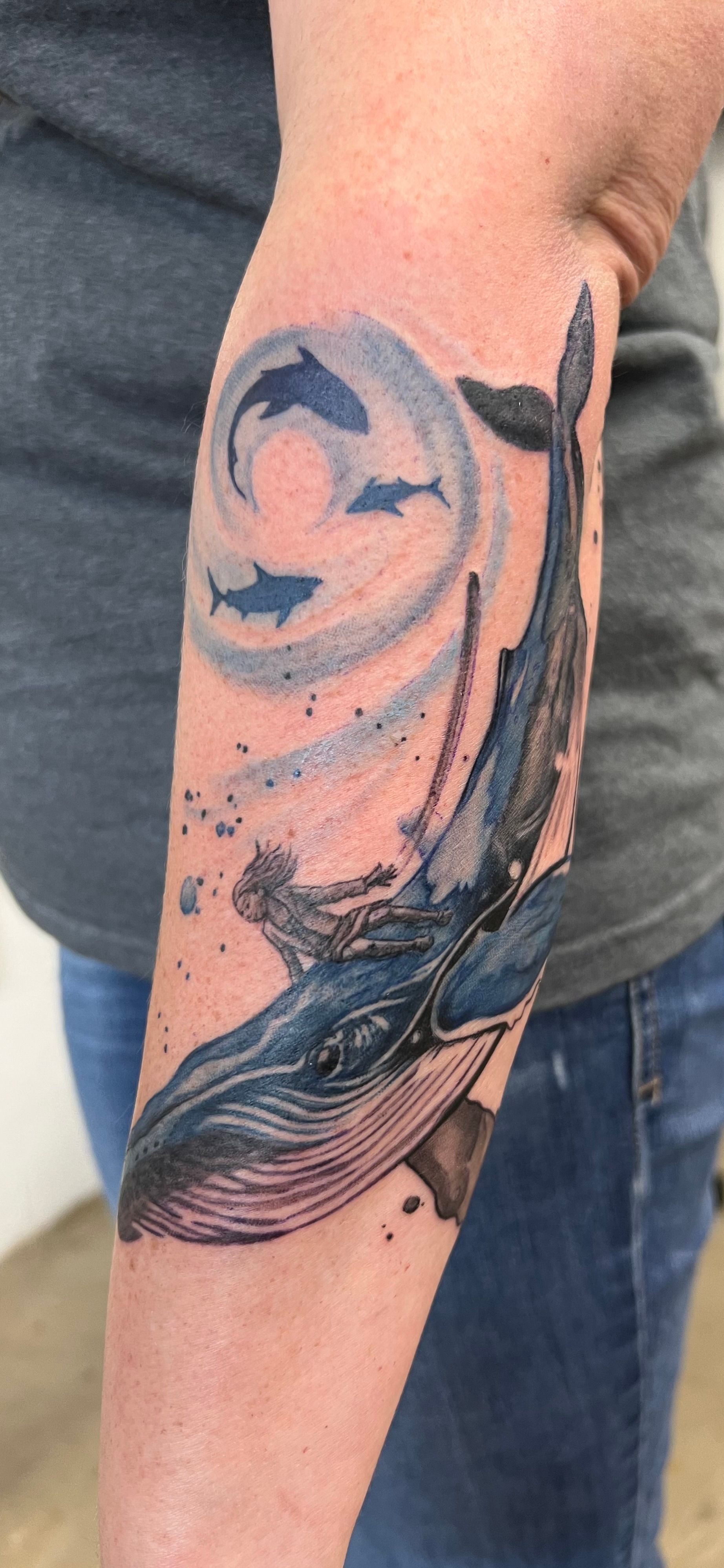 Tattoo of a whale and dolphins on a person's arm, featuring blue, gray, and black inks.