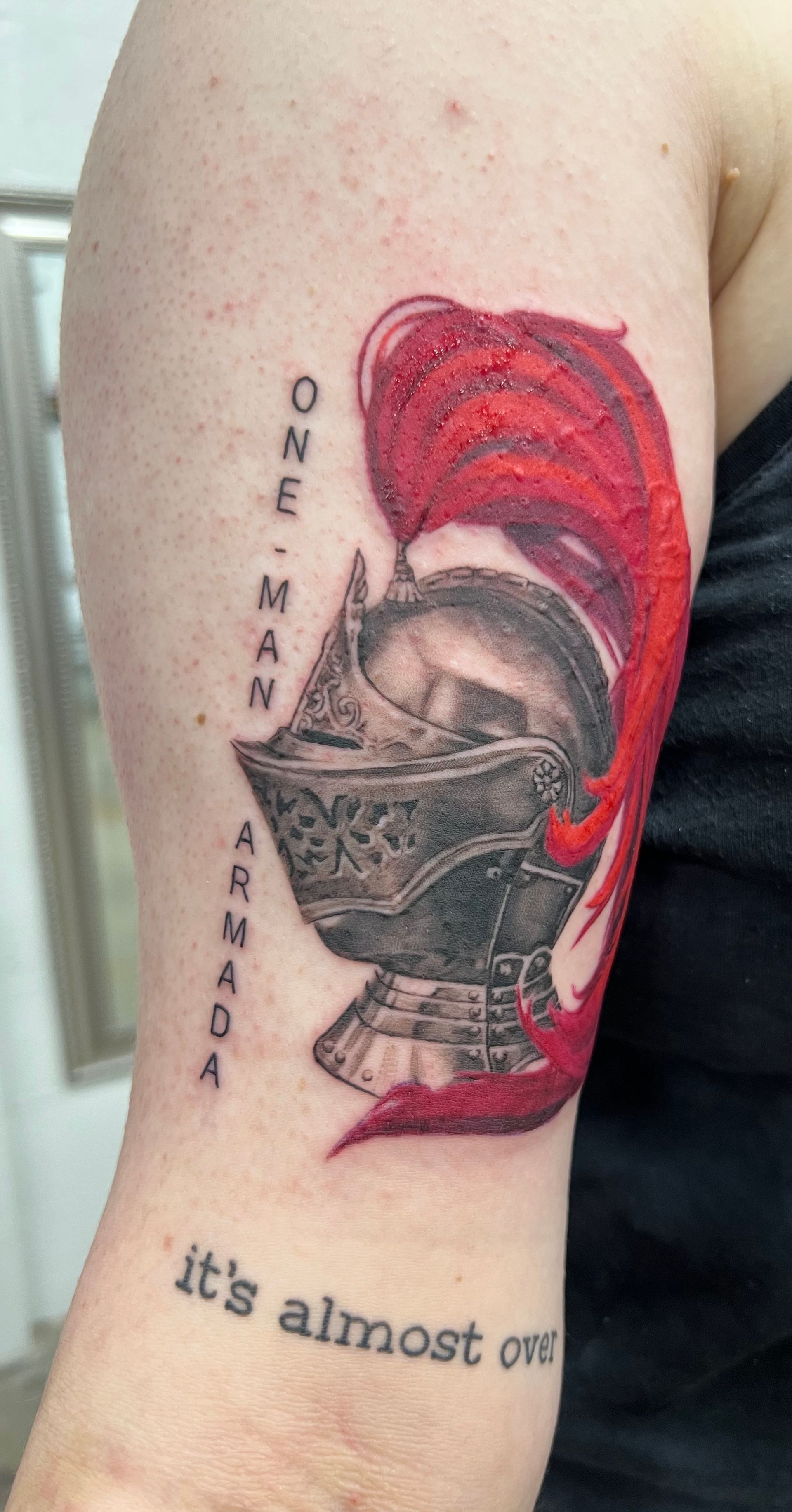 Tattoo of a knight's helmet with red plume and text