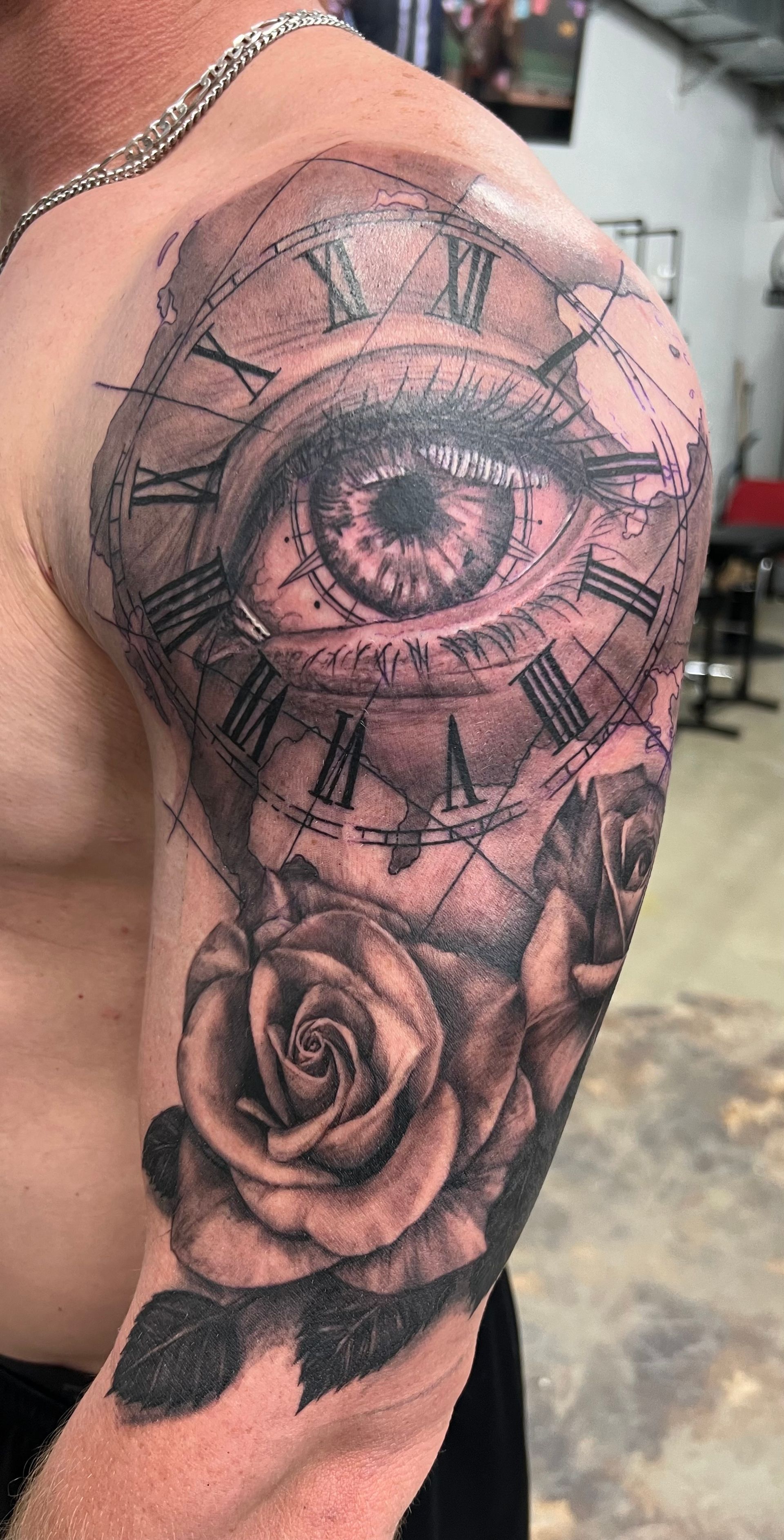 Tattoo of an eye within a clock design, with roses on the shoulder and upper arm.