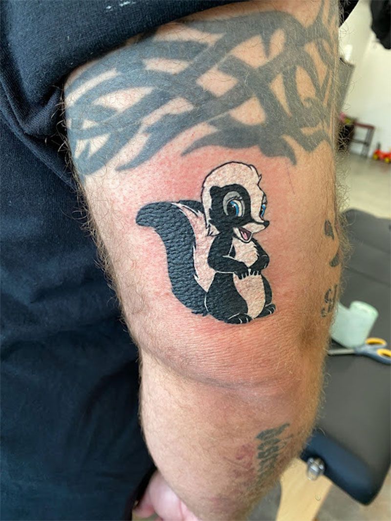 Tattoo of cartoon skunk with black and white body on a person's arm.