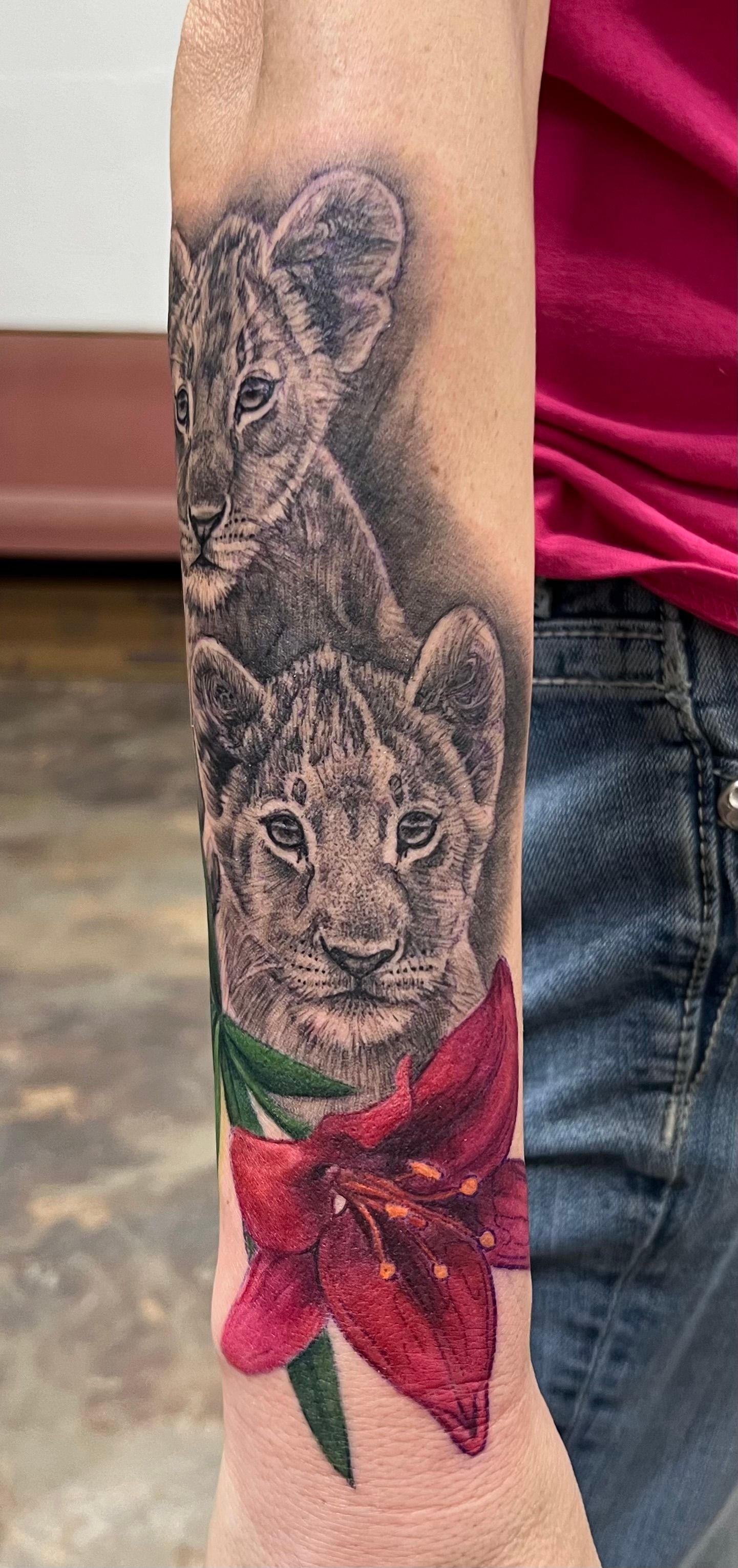 Tattoo of two lion cubs above a red lily on an arm, shaded background.