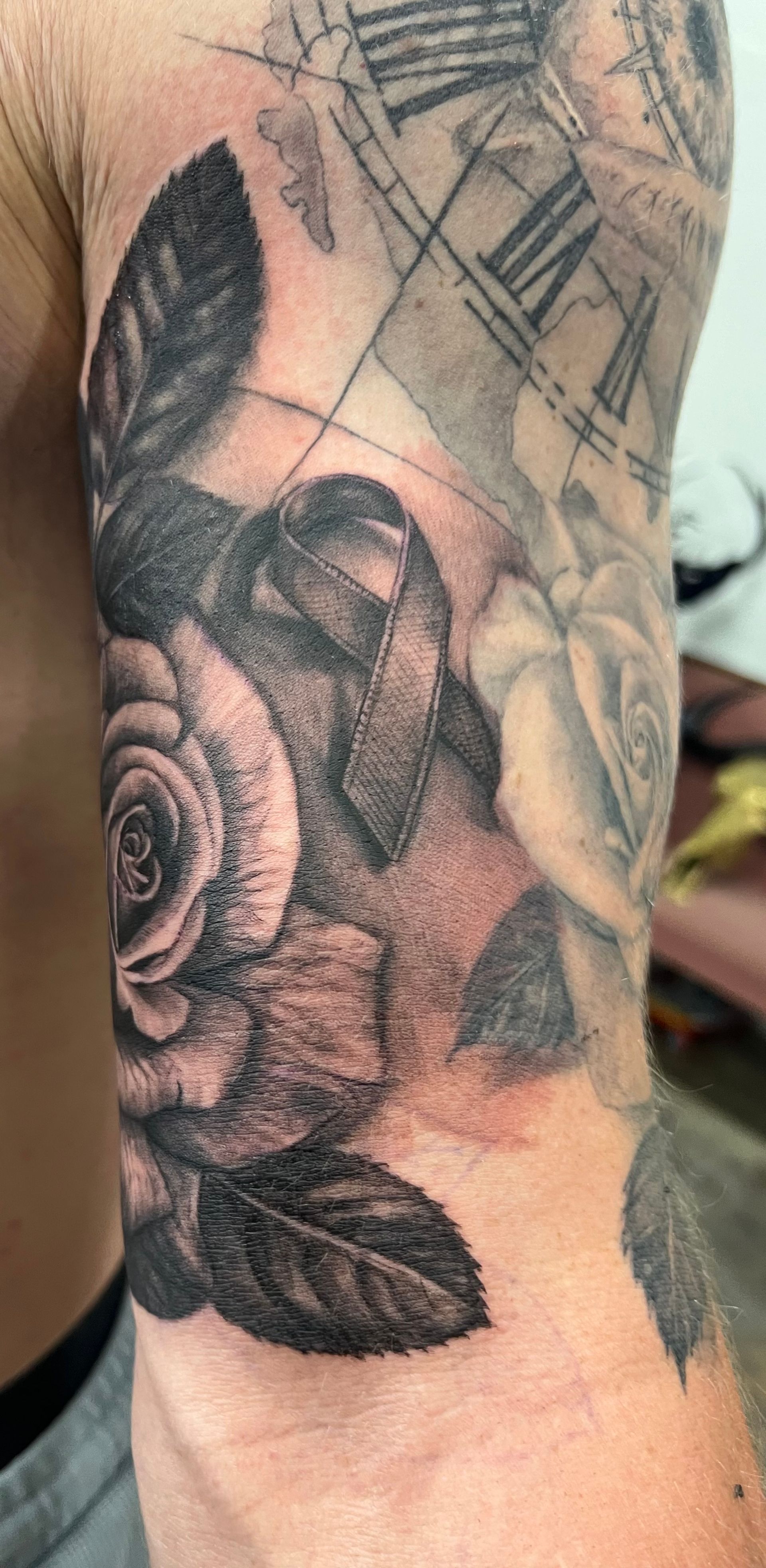 Tattoo on arm featuring rose and ribbon with clock background, in grayscale.