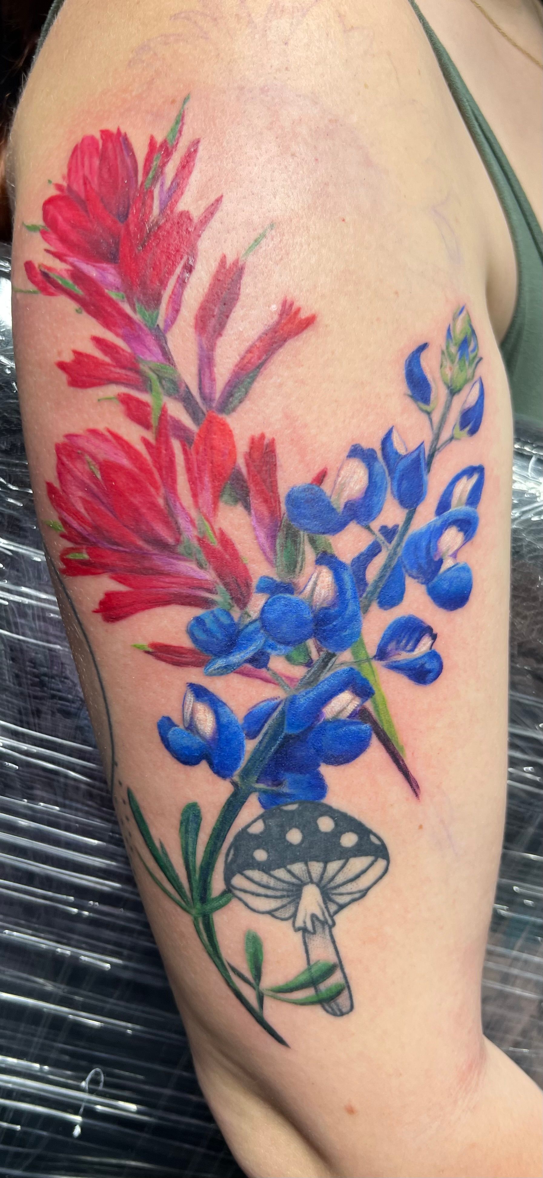 Tattoo of red and blue flowers with a mushroom on an arm.