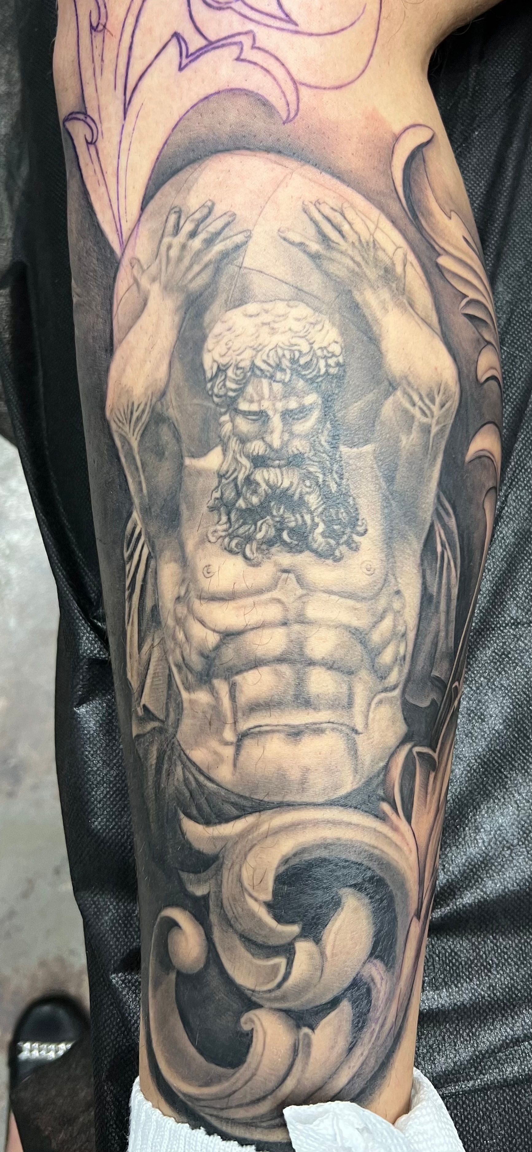 Tattoo of Atlas holding the world, surrounded by decorative filigree. Monochrome.