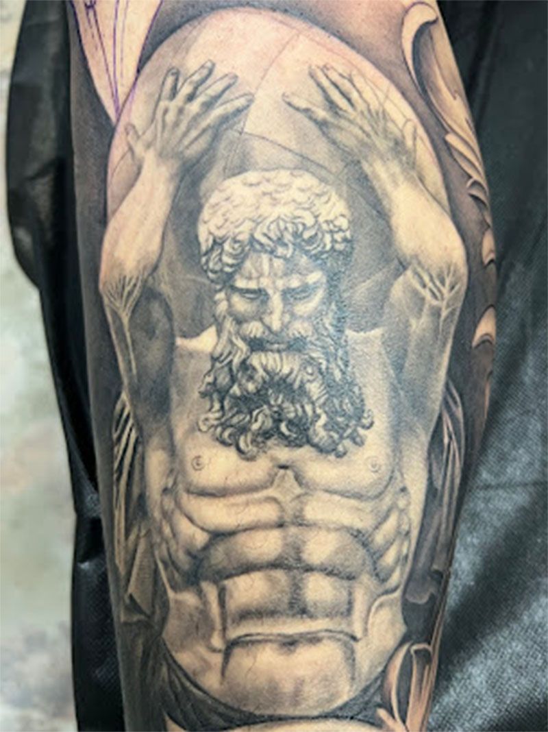 A man has a tattoo of a statue of atlas on his arm.