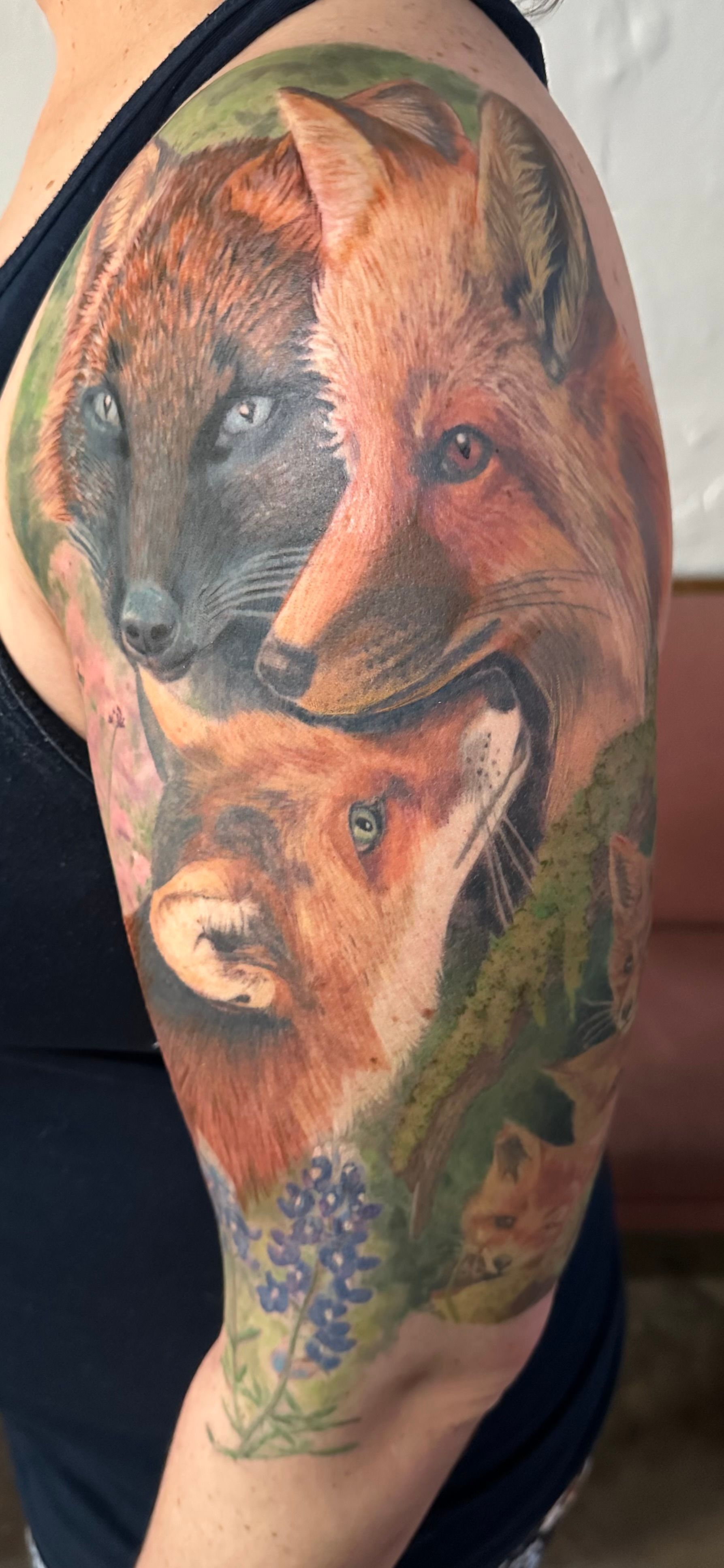 Tattoo of three foxes in vibrant colors, framed by green and purple foliage on a person's arm.