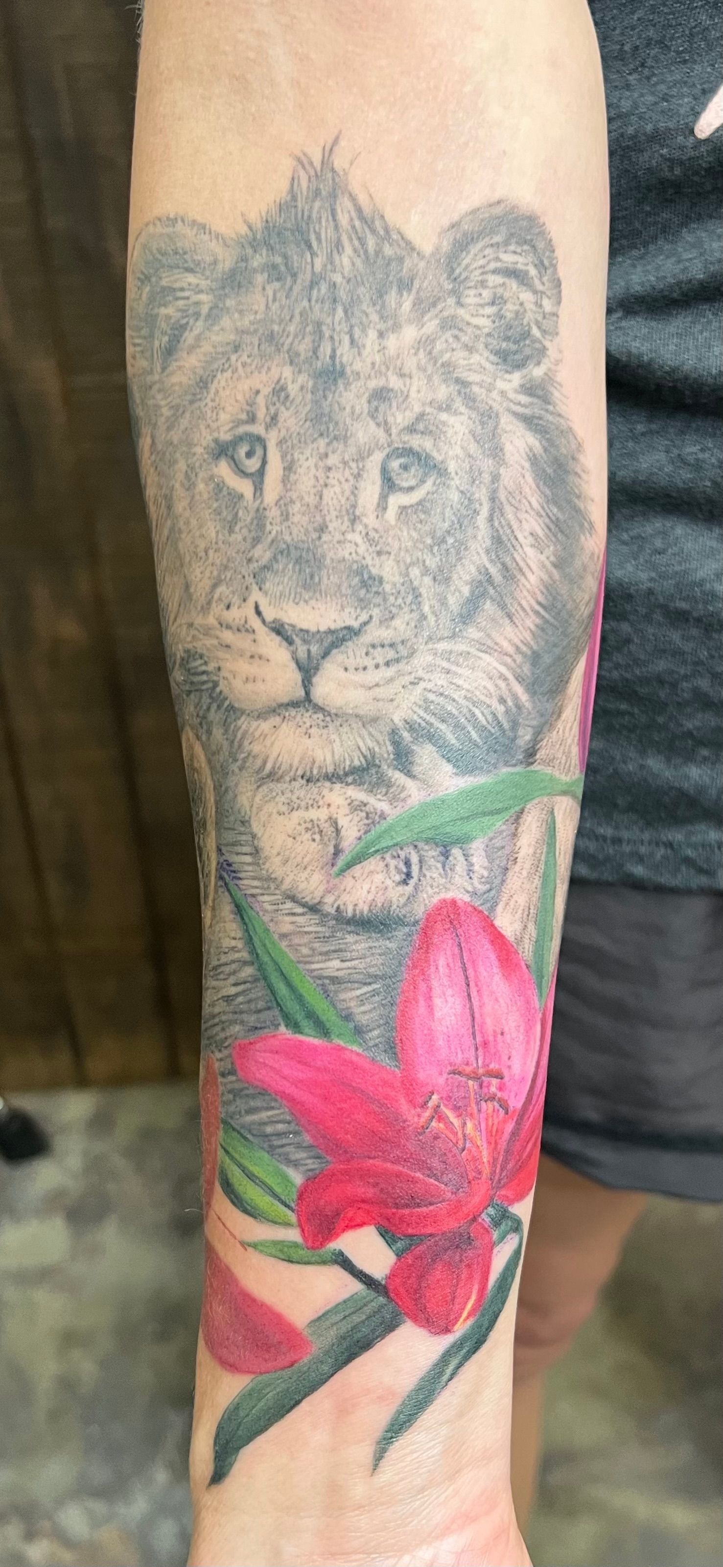 Lion tattoo on arm with red flowers.