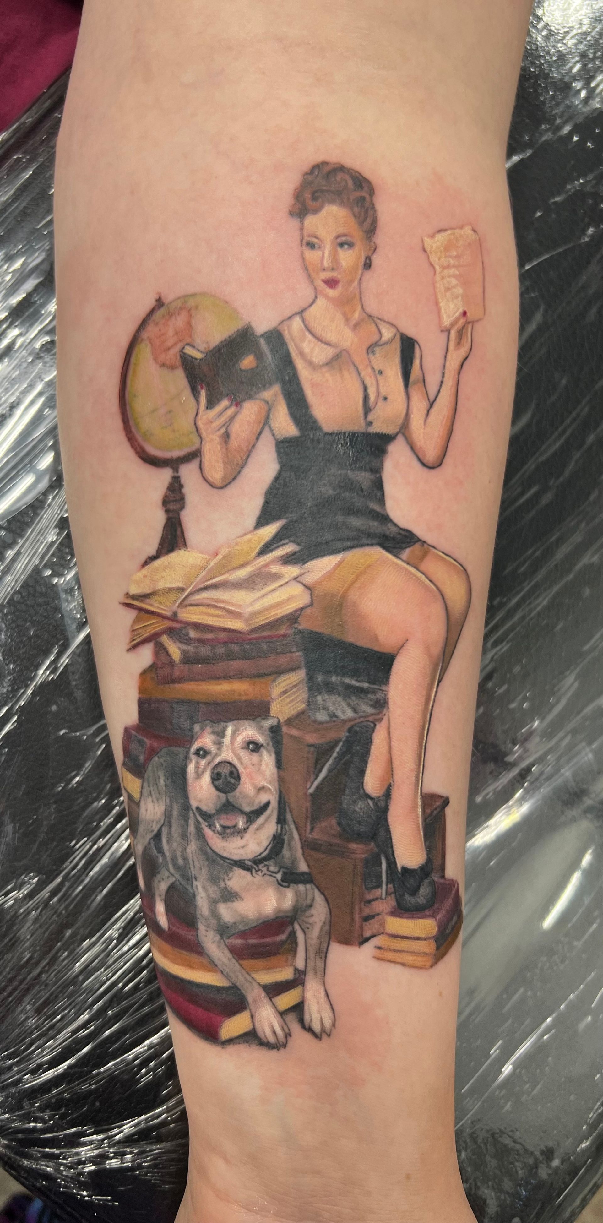 Tattoo of a woman in a vintage style reading, a dog in books, and a globe.