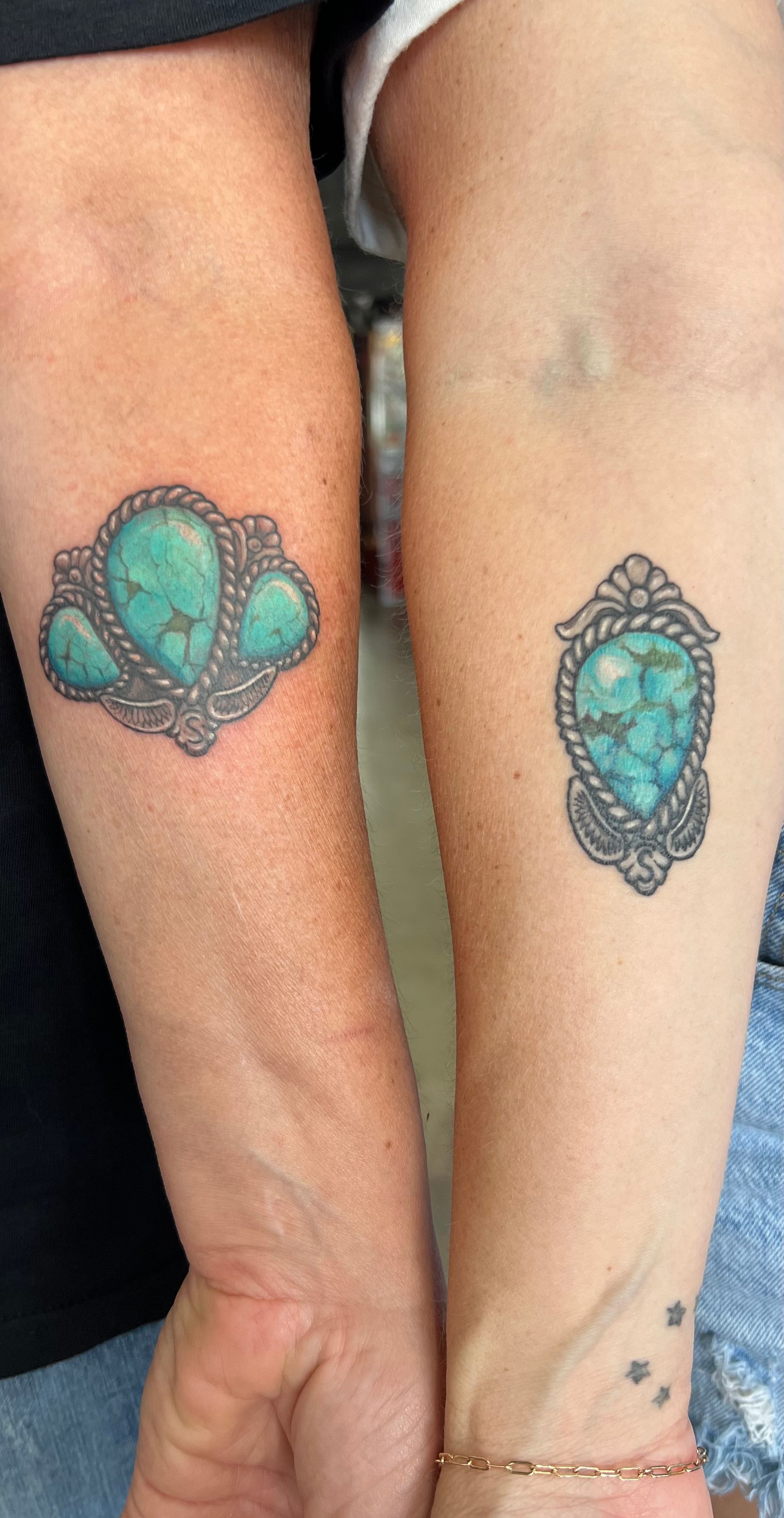 Two arms with matching turquoise gemstone tattoos on wrists, each with detailed silver settings.