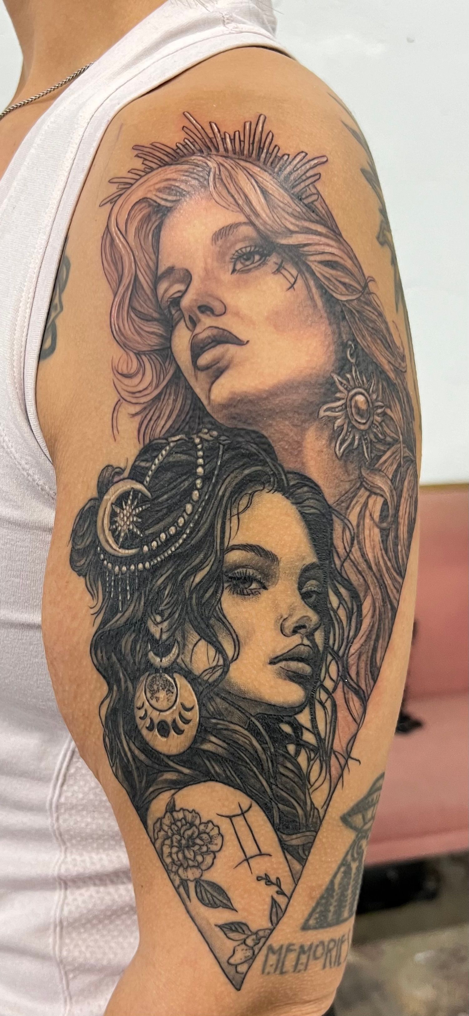Tattoo of two women's faces on arm. The lower one has jewelry and wavy hair; the upper one wears a crown.