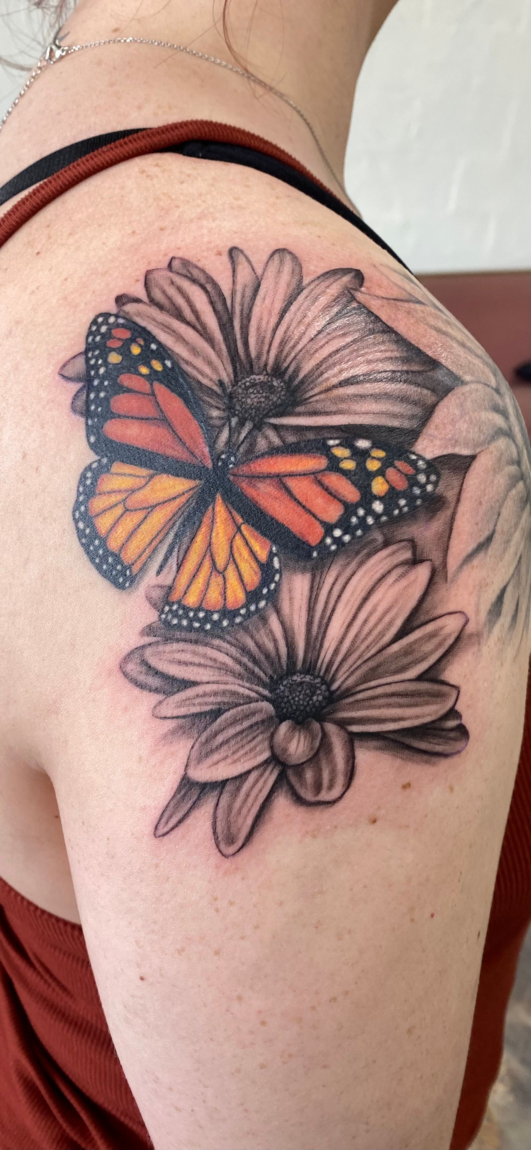 Tattoo of a monarch butterfly and daisies on a person's shoulder and arm.
