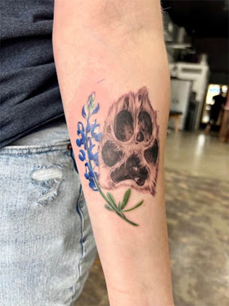 A person has a tattoo of a paw print and blue flowers on their forearm.