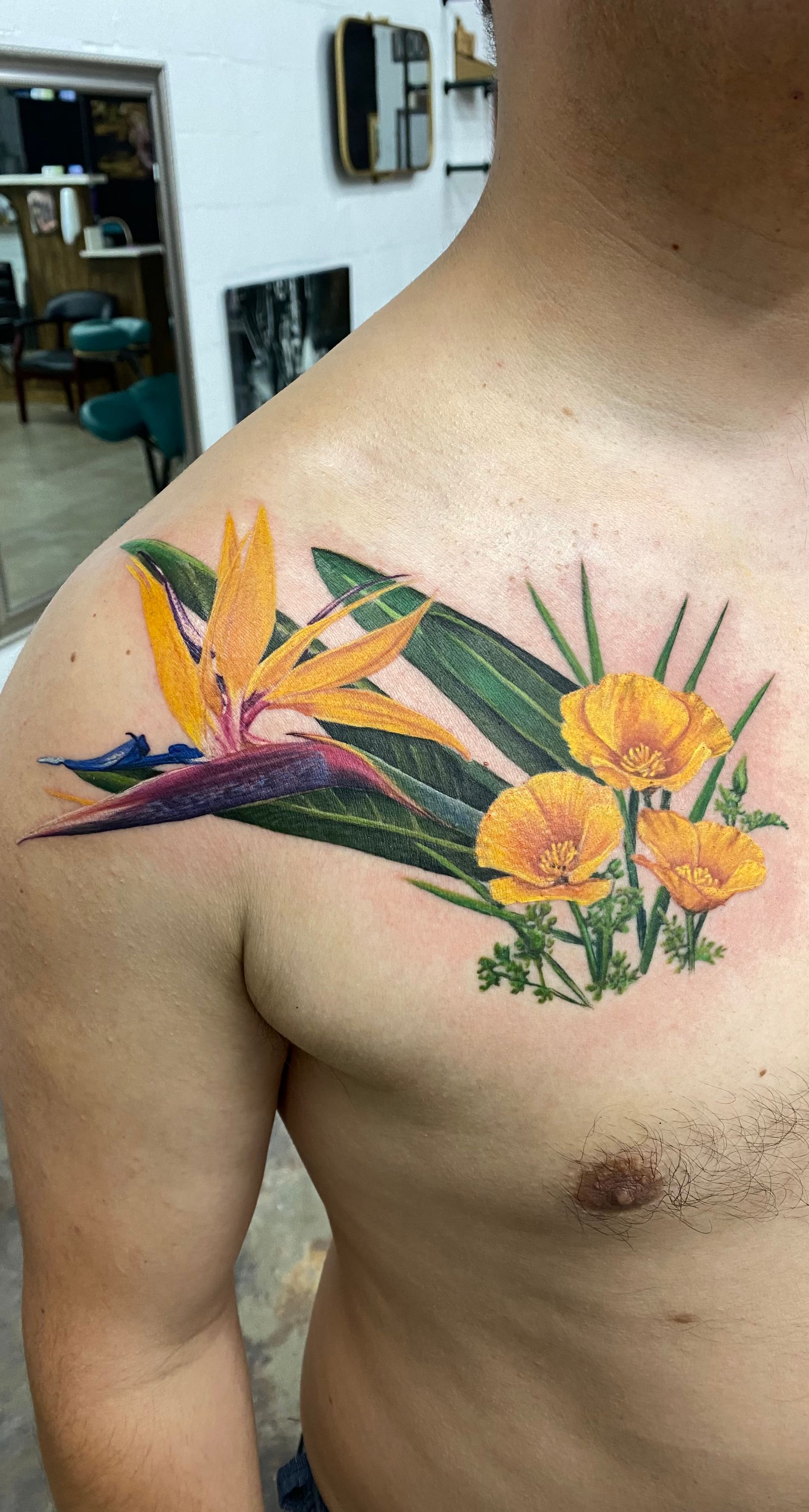 Tattoo of a bird of paradise flower and yellow blooms on a person's shoulder.