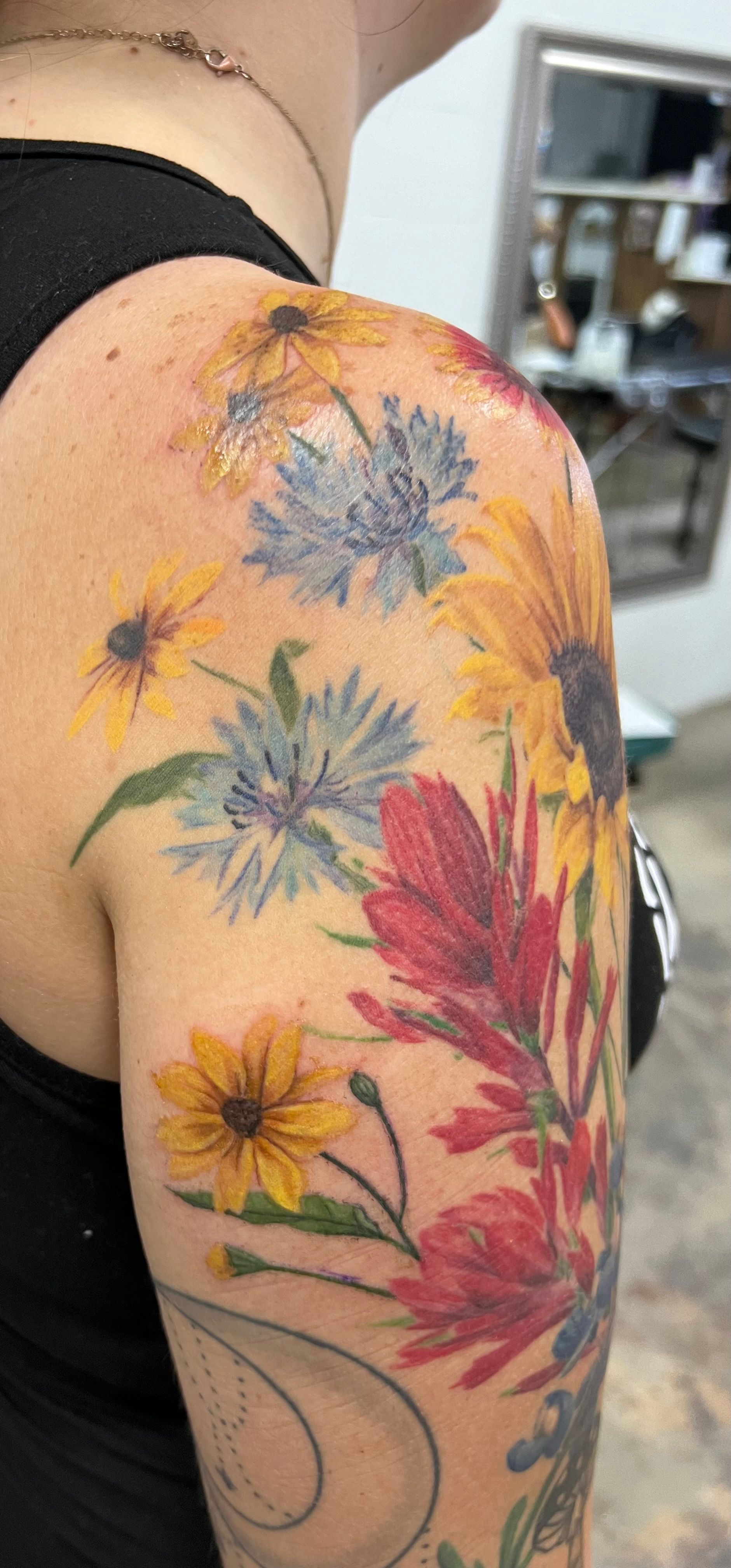 Tattoo of colorful wildflowers on a person's upper arm and shoulder.