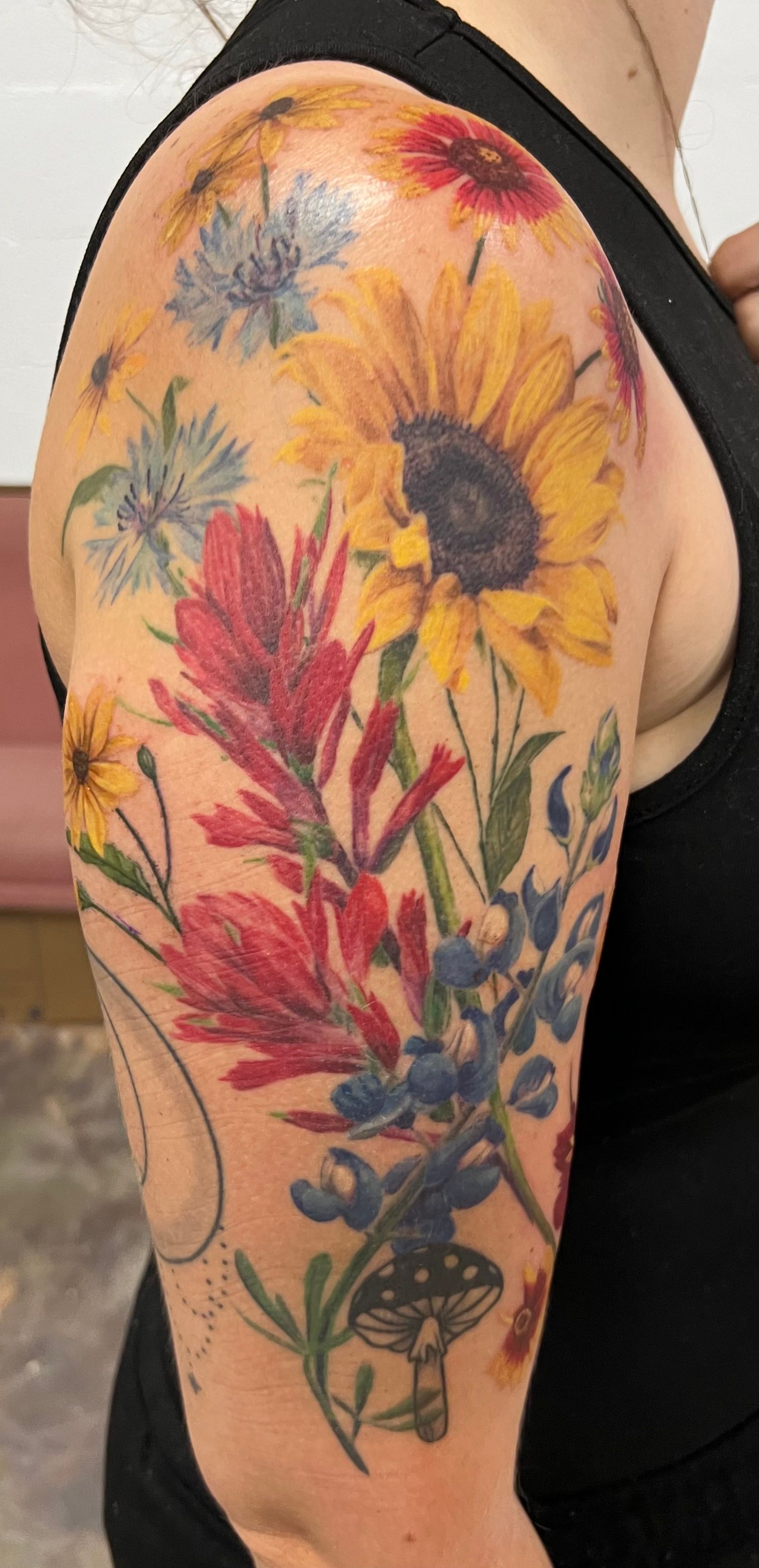 Tattoo of colorful wildflowers and a mushroom on a person's arm.